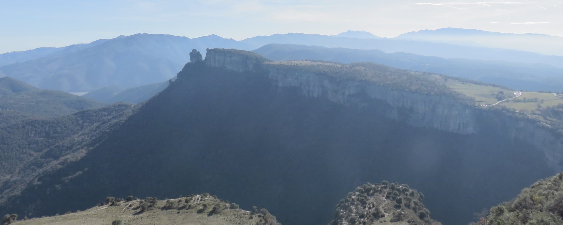 Abajo en el centro queda L’Agullola con el Pla de Fàbregues. Se aprecia el camino y parking a la derecha. Al fondo derecha queda el Montseny y a la izquierda Sant Miquel de Solterra o de Les Formigues
