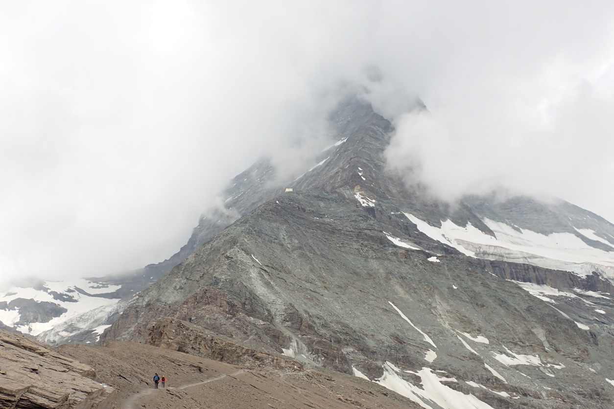 Subiendo al Refugio Hörnli, dicho refugio en mitad de la cresta, y detrás la cresta entre nubes hacia la cima del Cervino